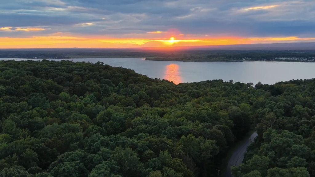 A drone shot taken above the trees from Phyllian's Bluff overlooking Saratoga Lake at sunset